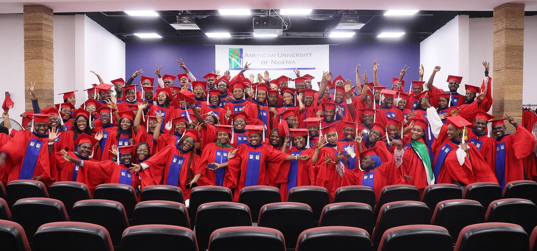 A graduating class in red gowns and caps celebrating at the American University of Nigeria